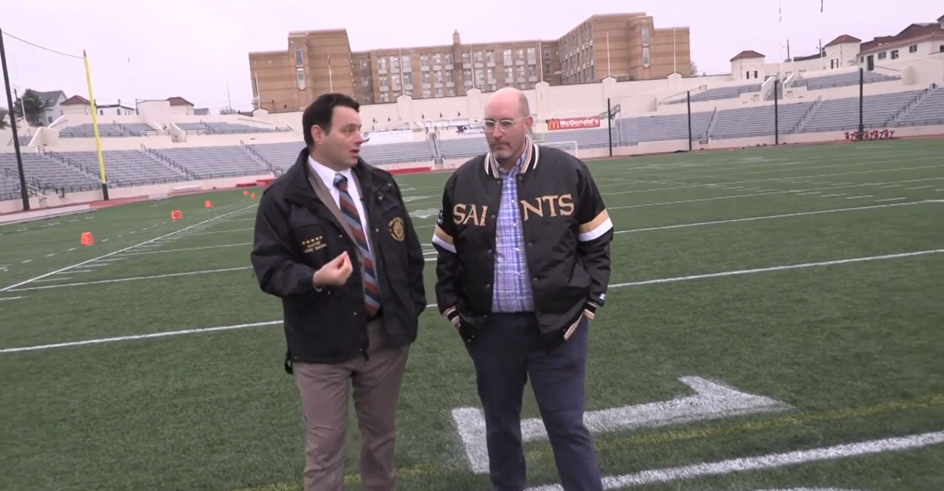 Mayor Andre Sayegh of Paterson, NJ walks on a football field with a reporter.